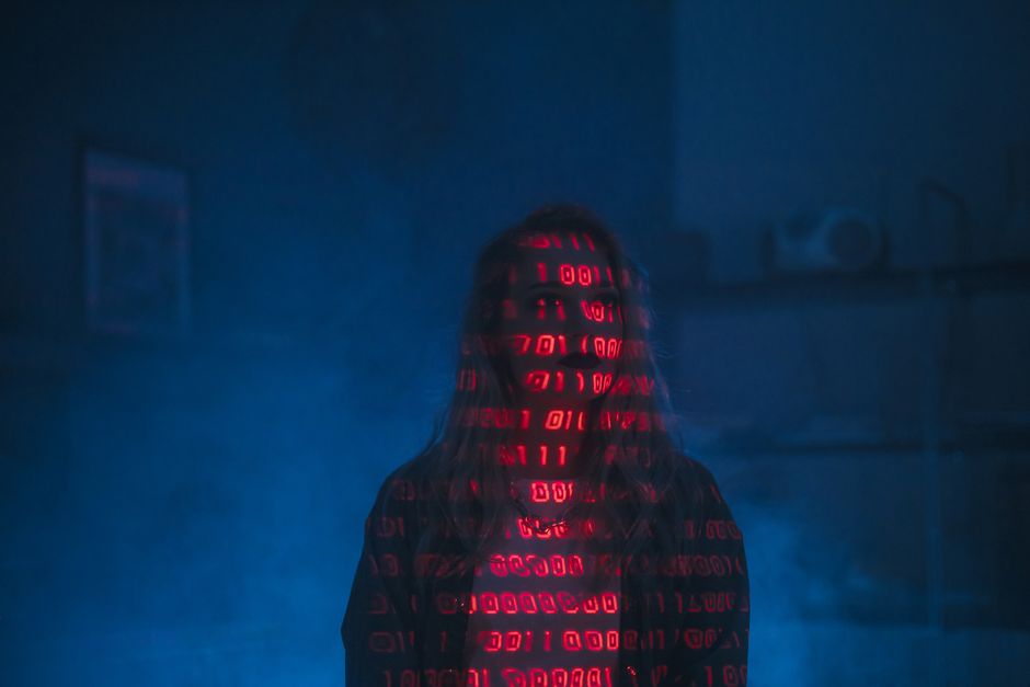 A pair of hands typing on a sleek, modern laptop displaying lines of code on a dark background, with the laptop placed on a dark surface. The scene suggests a focus on programming or digital work, wit